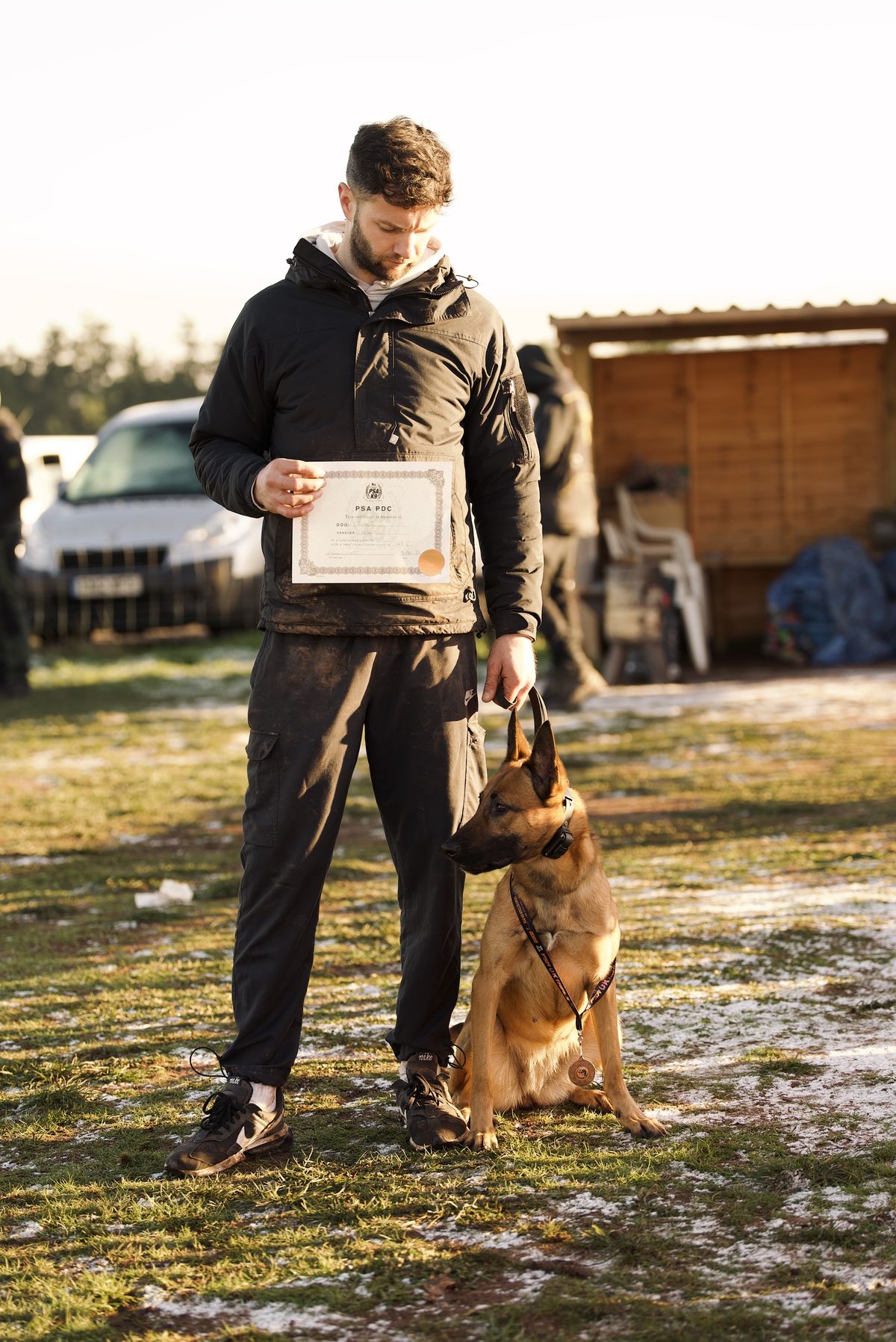 Jason standing with his Malinois at heel, holding a PSA certificate